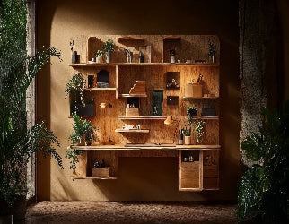 Modern wooden wall desk with shelves, decorated with plants and lamps, in a sunlit room for a stylish, functional home office space.