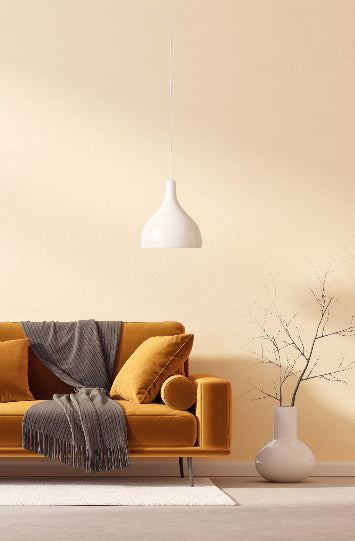 Modern living room with a mustard yellow sofa, gray throw blanket, white pendant lamp, and minimalist decor in warm tones.