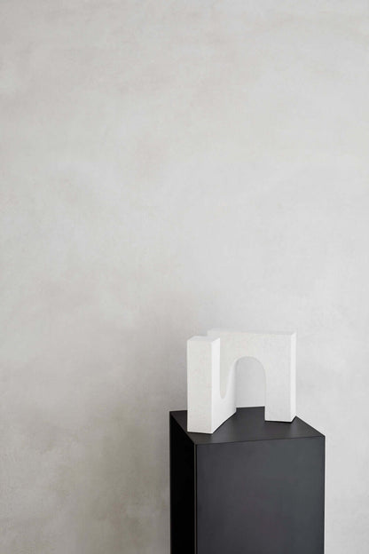 Alt Tag: Modern white sculpture on black pedestal against textured wall, perfect for luxury home decor and designer furniture settings.