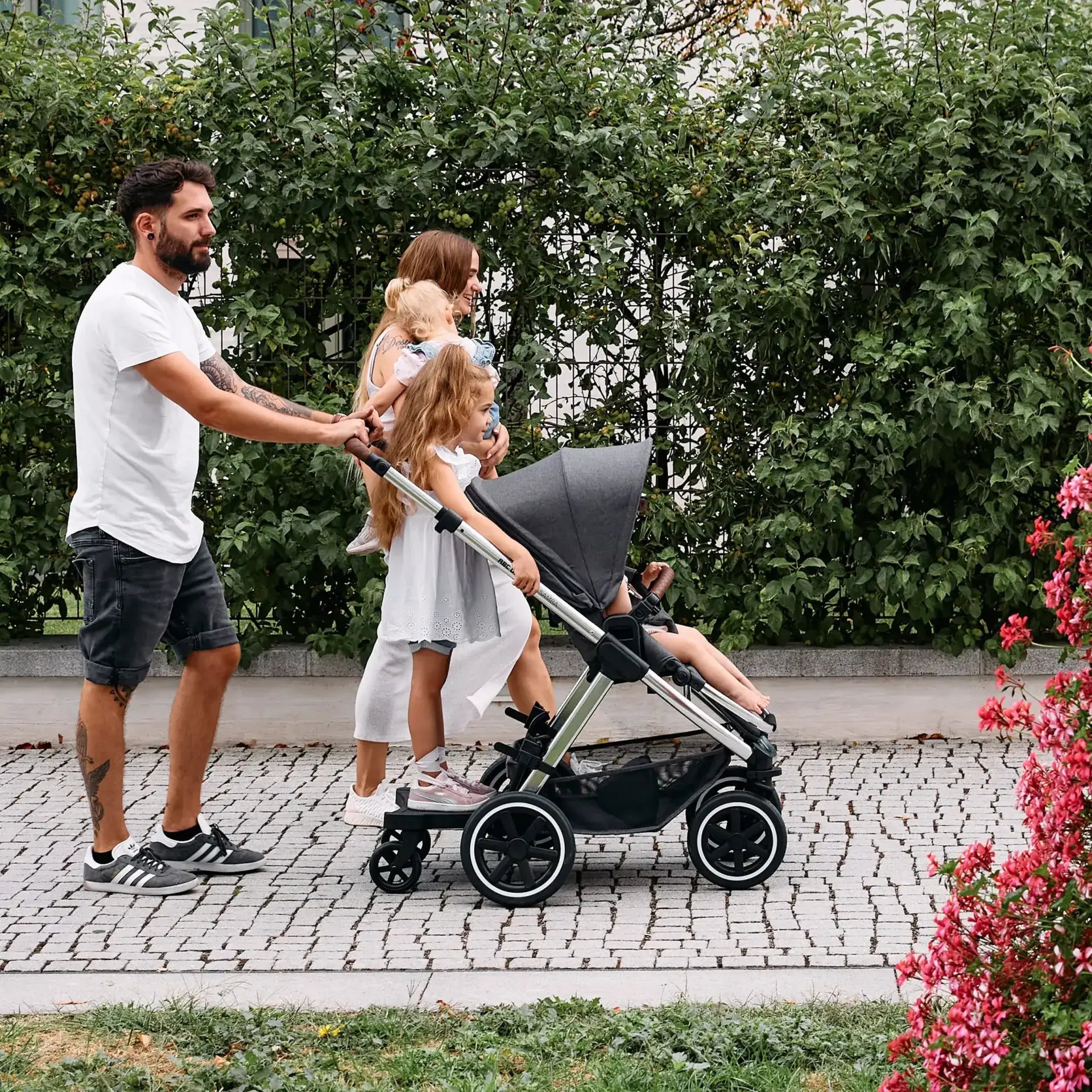 Family using ABC Design Kiddie Ride On 2 Board with stroller, showcasing luxury and modern furniture concepts in outdoor setting.