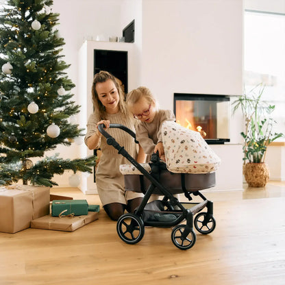 Mother and child enjoying a cozy moment with a stroller beside a Christmas tree and fireplace, showcasing holiday warmth and home decor elegance.