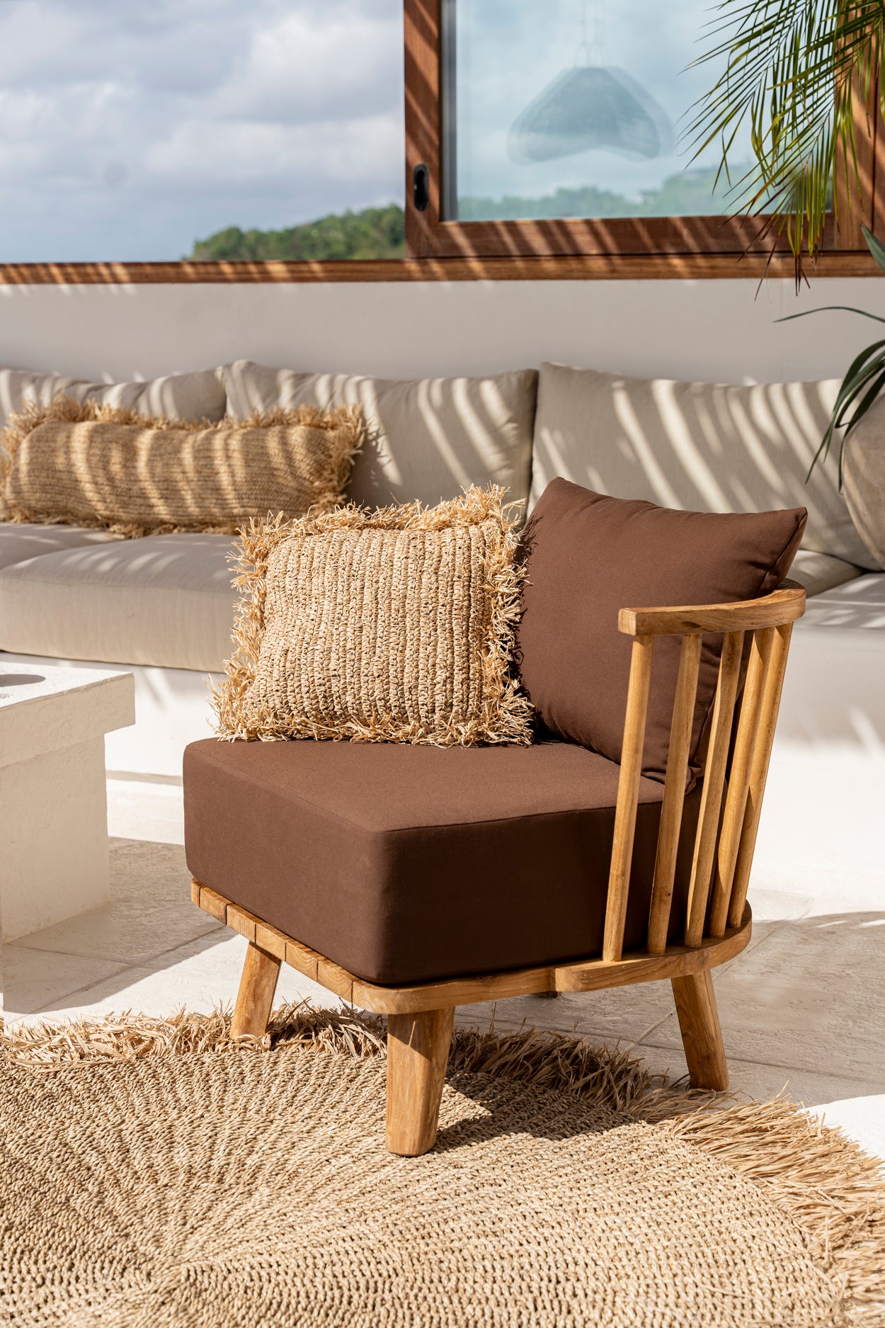 Outdoor patio with rustic wooden chair, brown cushions, and woven rug, creating a cozy and serene relaxing space.