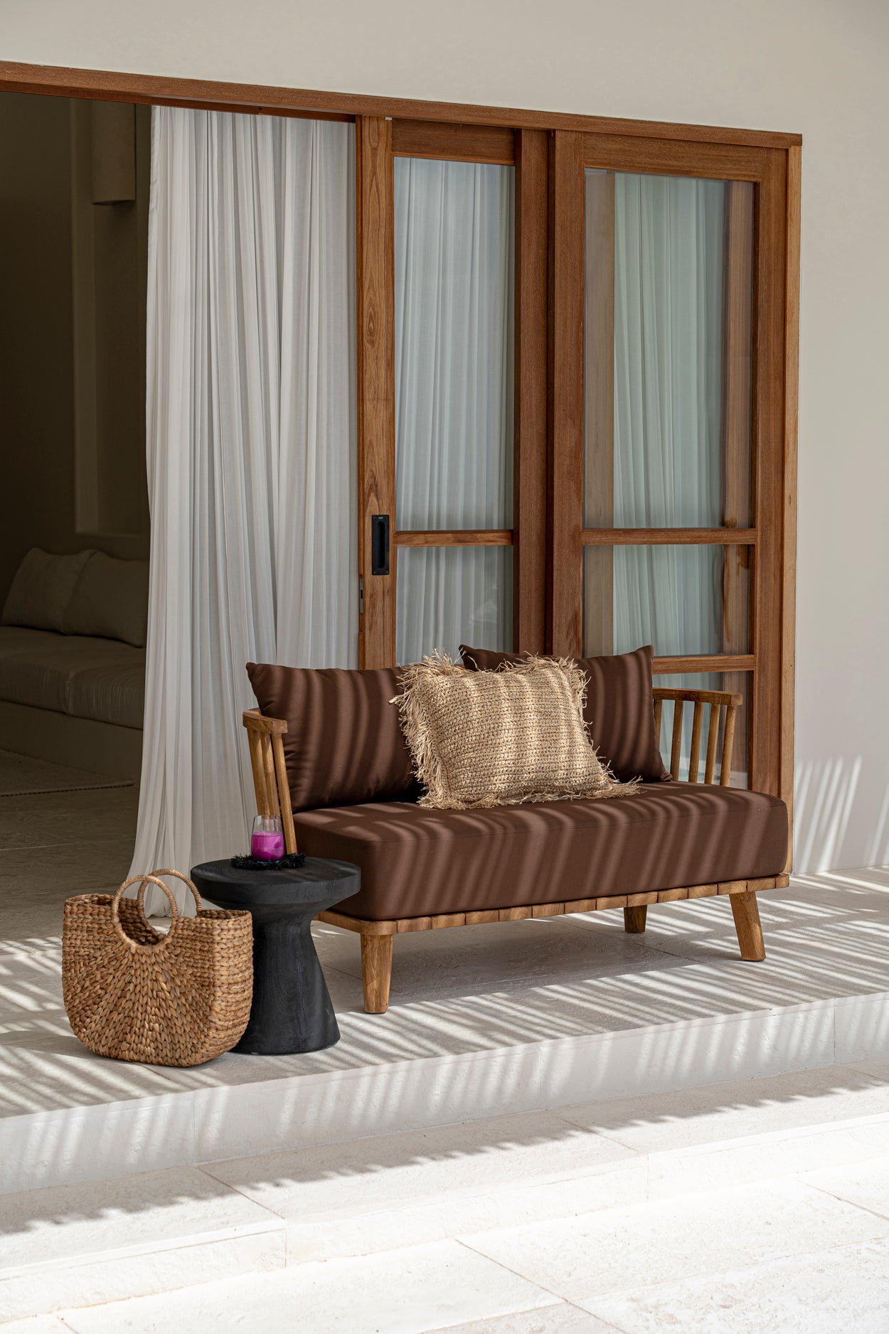 Stylish outdoor seating area with wooden lounge chair, woven cushion, and a basket beside a sliding glass door.