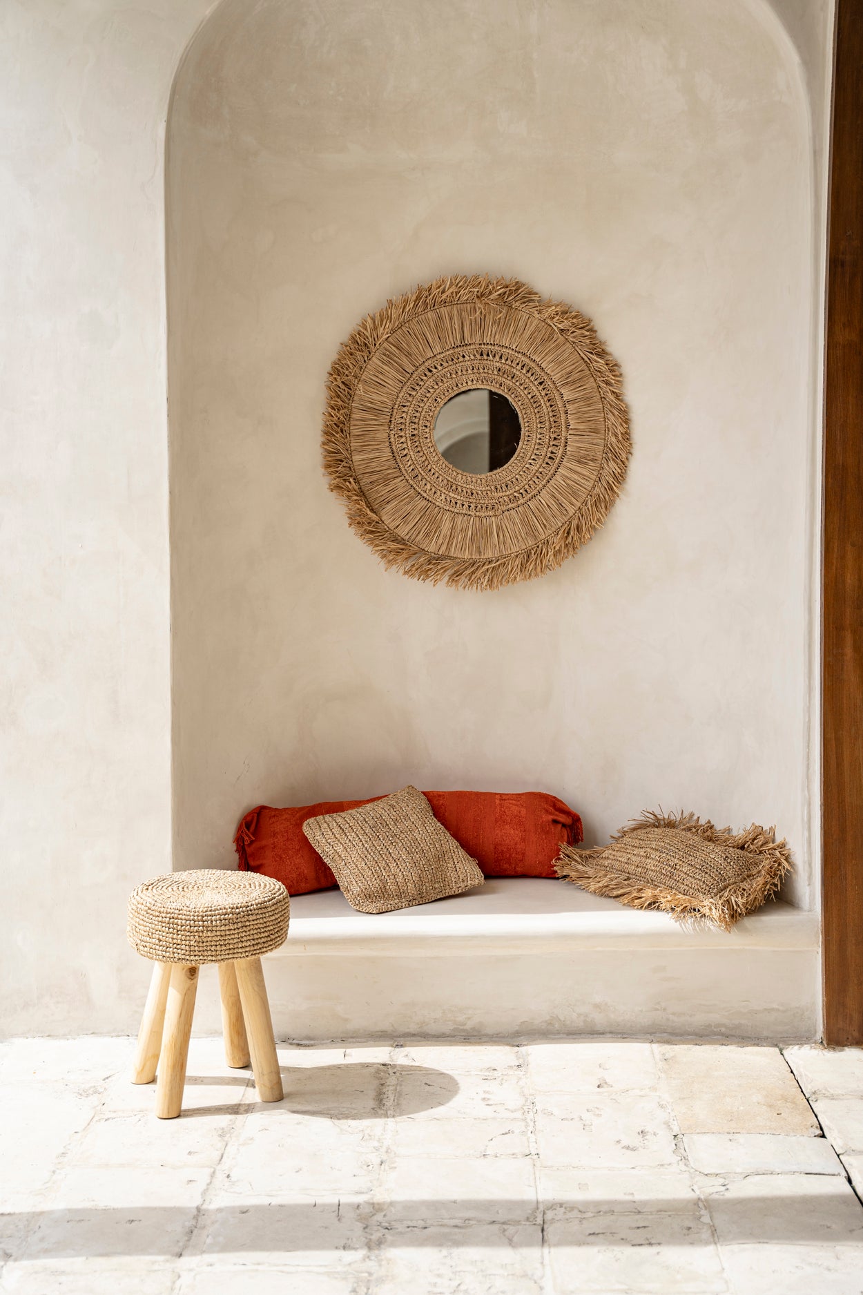 Bohemian chic interior with woven mirror, cushions, and rustic stool in natural tones, creating a serene and inviting atmosphere.