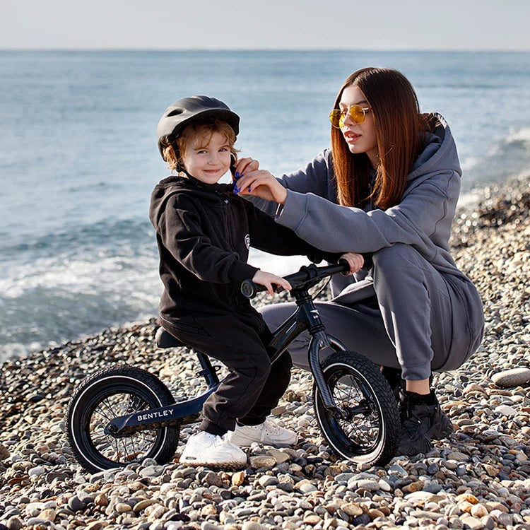 Mother adjusts child's helmet on a balance bike at a pebble beach.