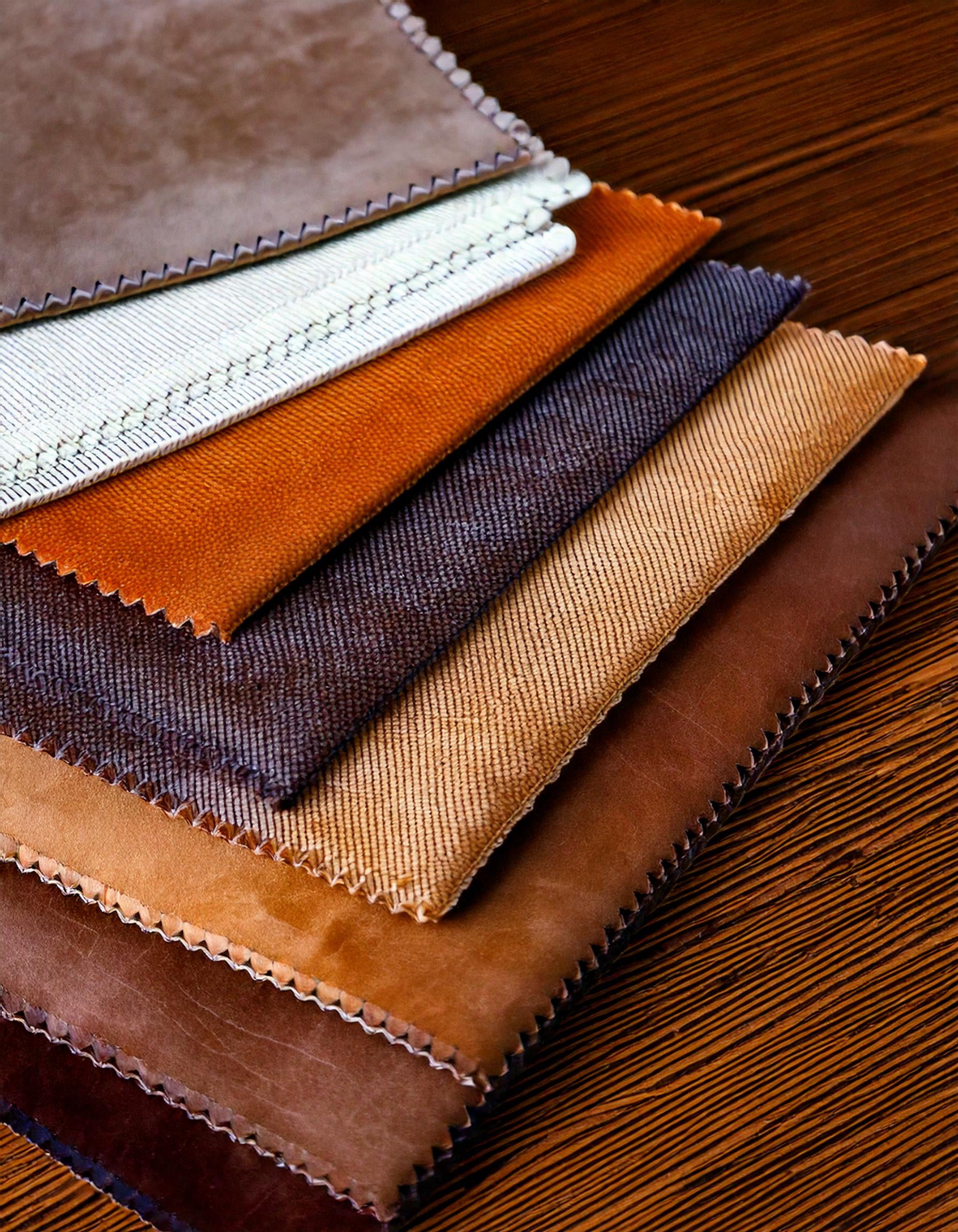 Assorted fabric swatches in brown, orange, and cream tones on a wooden surface.