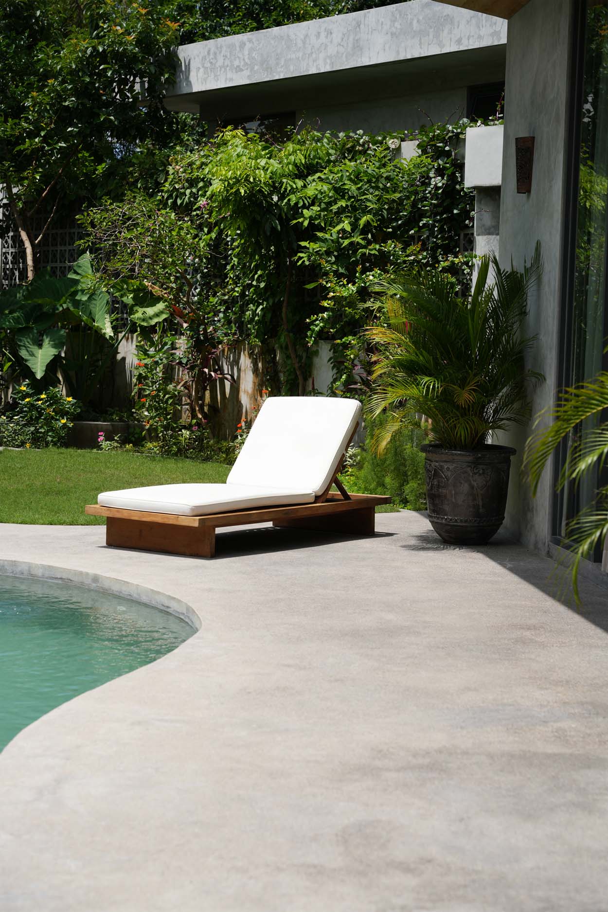 Luxury outdoor lounge chair by the pool surrounded by lush green plants, offering a relaxing garden retreat.
