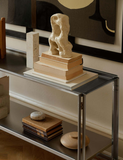 Luxury foldable console in brushed stainless steel with books and sculptures, modern furniture for high-end home decor.