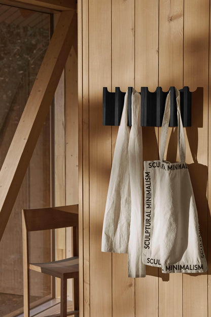 Minimalist wooden interior featuring a designer chair and tote bags on a black wall hook.