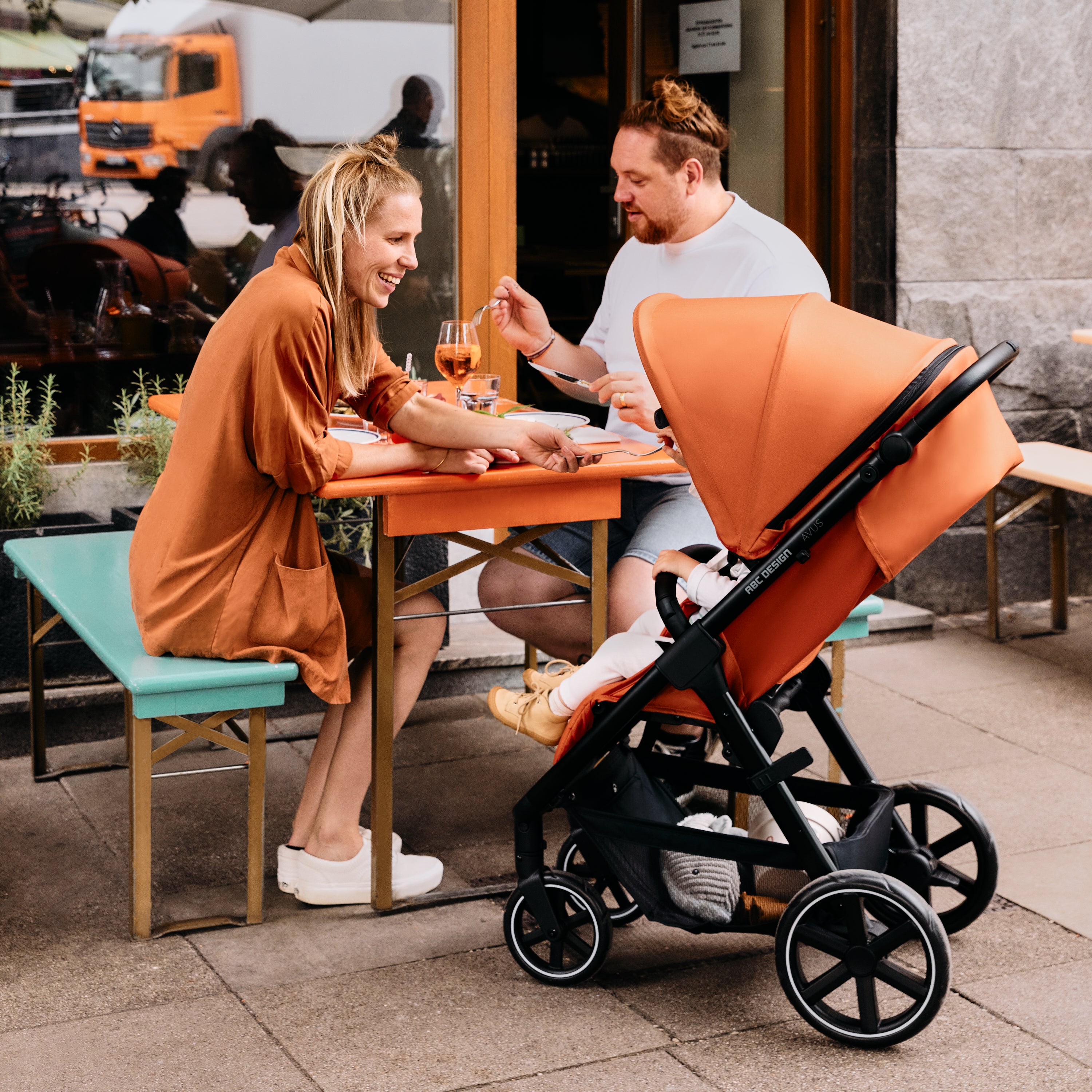Couple enjoying a meal outdoors with a stroller beside their table